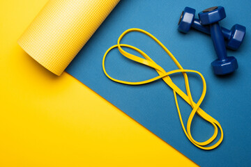 top view of blue fitness mat with dumbbells and resistance band on yellow background