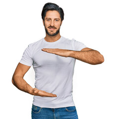Young hispanic man wearing casual white t shirt gesturing with hands showing big and large size sign, measure symbol. smiling looking at the camera. measuring concept.