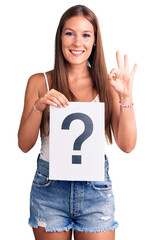 Young beautiful hispanic woman holding question mark doing ok sign with fingers, smiling friendly gesturing excellent symbol