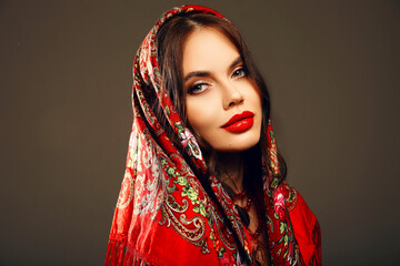 Russian girl Matryoshka style. Fashion woman portrait with traditional red headscarf. Beauty girl model with red lips makeup isolated on studio background. - 775210008