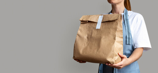 Waitress holds brown package bag for takeout food in her hands. Takeaway food online order. 