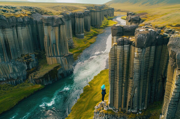  Iceland's mysterious basalt columns with woman standing on one in the middle looking down into deep blue river below - obrazy, fototapety, plakaty