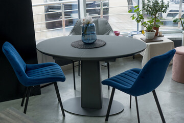 Gray wooden table combined with blue wooden chairs with soft fabric upholstery. There is a blue glass vase with flowers on the table