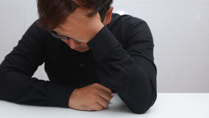 depressed young man sitting at the table and covering his face with his hands