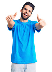 Young handsome man with beard wearing casual t-shirt approving doing positive gesture with hand, thumbs up smiling and happy for success. winner gesture.