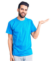 Young handsome man with beard wearing casual t-shirt smiling cheerful presenting and pointing with palm of hand looking at the camera.