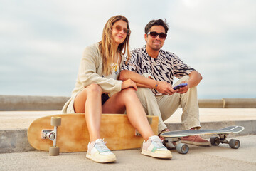 heterosexual couple sitting on sidewalk with skateboards hanging out happy