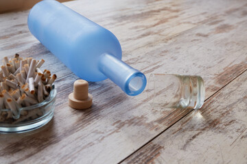 An overturned bottle of alcohol, an overturned glass, and an ashtray full of cigarette butts on the...