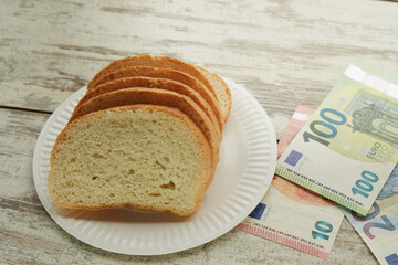 Bread on a plate on the table next to euro bills of different denominations, rising food prices in Europe - obrazy, fototapety, plakaty