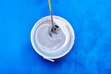 Top view captures process of stirring rod mixing fresh, white paint in bucket.