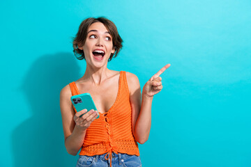 Portrait of impressed girl wear orange knit top look at awesome offer empty space hold smartphone isolated on blue color background