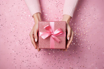  glamorous pink background with woman hands holding a wrapped gift box seen from above for a birthday 