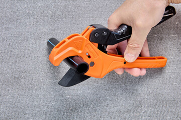 Pipe scissors cutter hand plumbing tool for cutting HDPE pipes, close-up on gray background.
