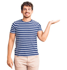 Young handsome man with curly hair wearing casual clothes smiling cheerful presenting and pointing...