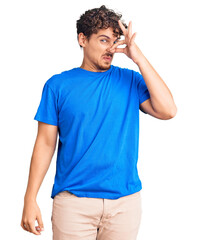 Young handsome man with curly hair wearing casual clothes smelling something stinky and disgusting,...