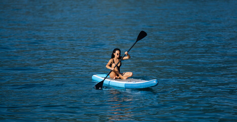 Beautiful young woman relaxing on paddle board in the summer lake or sea water. Luxury summer resort. Sexy sensual fit woman rest in water. Beautiful model enjoying summer travel vacation. - obrazy, fototapety, plakaty