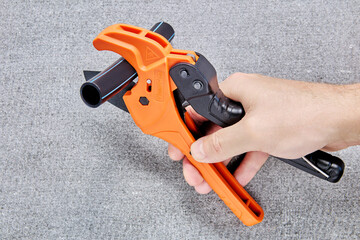 Ratcheting pipe cutter in shape of scissors with polyethylene tube on blade is held in hand of...