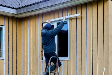 Exterior finishing work on frame and panel house on facade side, roofer installs window opening...