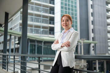 Portrait of a happy Asian Businesswoman with arms crossed and looking at the camera standing near her office, with a big building background.