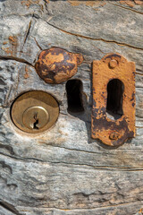 Close-up of rusty antique keyhole next to modern lock on weather-worn wood of an antique wooden door