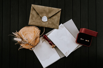 A flat lay composition of wedding items on a dark wooden surface, featuring a sealed envelope, a...