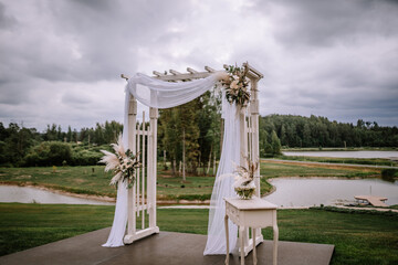 Valmiera, Latvia - Augist 13, 2023 - An elegant outdoor wedding arch adorned with white fabric and...