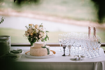A wedding cake on a table with plates and glasses, with a bouquet and champagne bottles in the...
