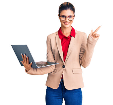 Young beautiful woman holding laptop smiling happy pointing with hand and finger to the side