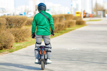 Man riding EUC electric wheel on sidewalk. Man commuting on electric monowheel with protective gear, ensure safety while riding. City mobility with unicycle,  eco-friendly urban transport.