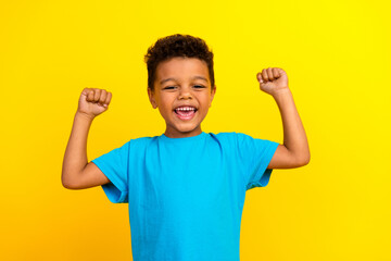 Portrait of cute small schoolboy with afro hair wear blue stylish t-shirt scream yeah raising fists...