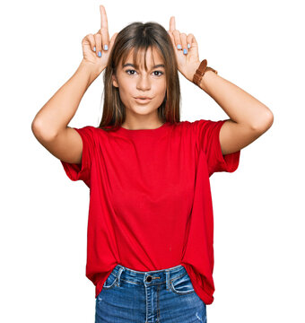 Teenager caucasian girl wearing casual red t shirt doing funny gesture with finger over head as bull horns