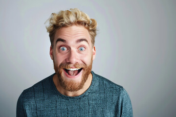 A very excited, surprised man looks at the camera with his mouth open, isolated on a light gray background. A funny-looking red-haired and bearded man. Live emotions. Idea for advertising. Copy space - obrazy, fototapety, plakaty