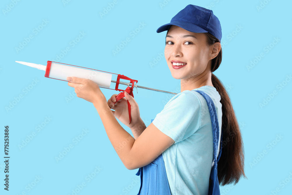 Sticker Female Asian plumber with caulking gun on blue background