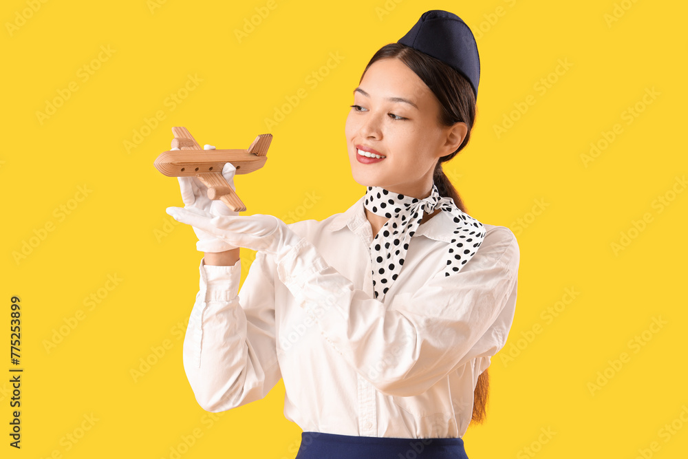 Sticker Beautiful Asian stewardess with wooden airplane on yellow background