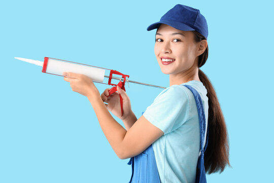 Female Asian plumber with caulking gun on blue background