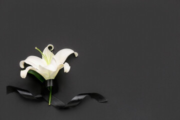 Beautiful lily flowers with black funeral ribbon on dark background