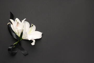 Beautiful lily flowers with black funeral ribbon on dark background