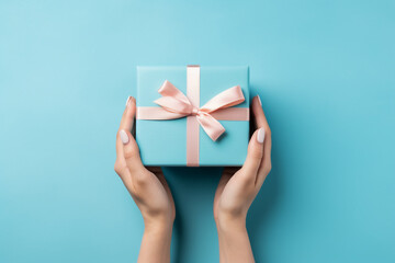 Minimal blue background with woman hands holding a wrapped gift box seen from above for a birthday 