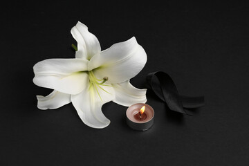 Beautiful lily flower with burning candle and black funeral ribbon on dark background