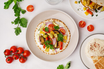 Plates of tasty pita bread with grilled vegetables on white background