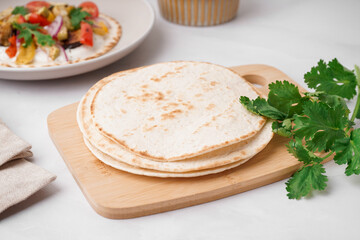Wooden board of tasty pita bread on white background