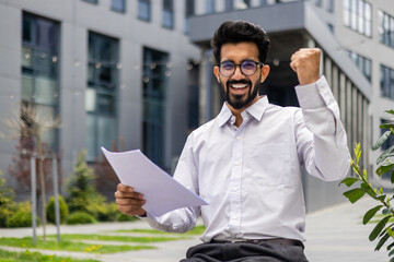 Portrait of a happy Indian male businessman smiling at the camera and happy reading a letter and...