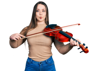 Young hispanic girl playing violin making fish face with mouth and squinting eyes, crazy and comical.