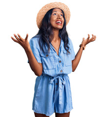 Young indian girl wearing summer hat crazy and mad shouting and yelling with aggressive expression and arms raised. frustration concept.
