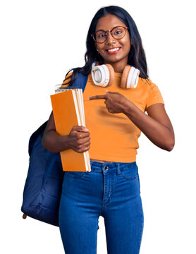 Young indian girl holding student backpack and books smiling happy pointing with hand and finger