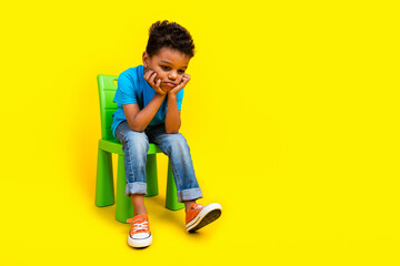 Full size photo of sad little schoolboy wear blue t-shirt sitting on chair look down empty space...