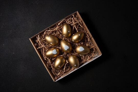 Gold eggs in paper box on black background. Top view.