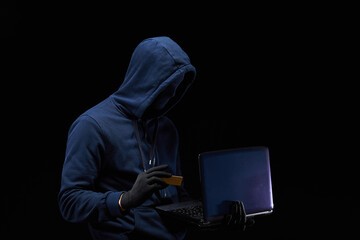 A hacker holding a credit card steals money using a laptop. A male thief hacks into highly secure...