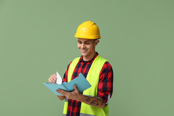 Young male engineer with clipboard on green background