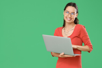 Young woman in eyeglasses using laptop on green background